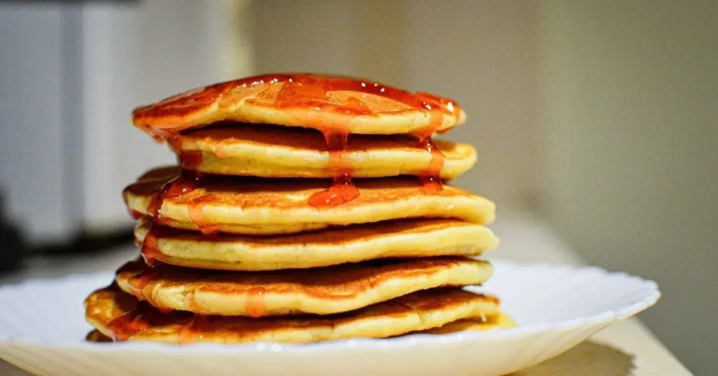 A stack of golden Kodiak pancakes topped with drizzled syrup on a white plate.