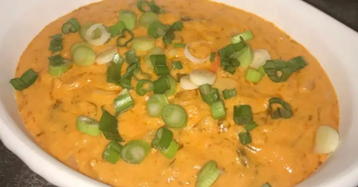 A skillet of creamy smoked queso topped with diced tomatoes, green chilies, red onions, and fresh cilantro, surrounded by tortilla chips.