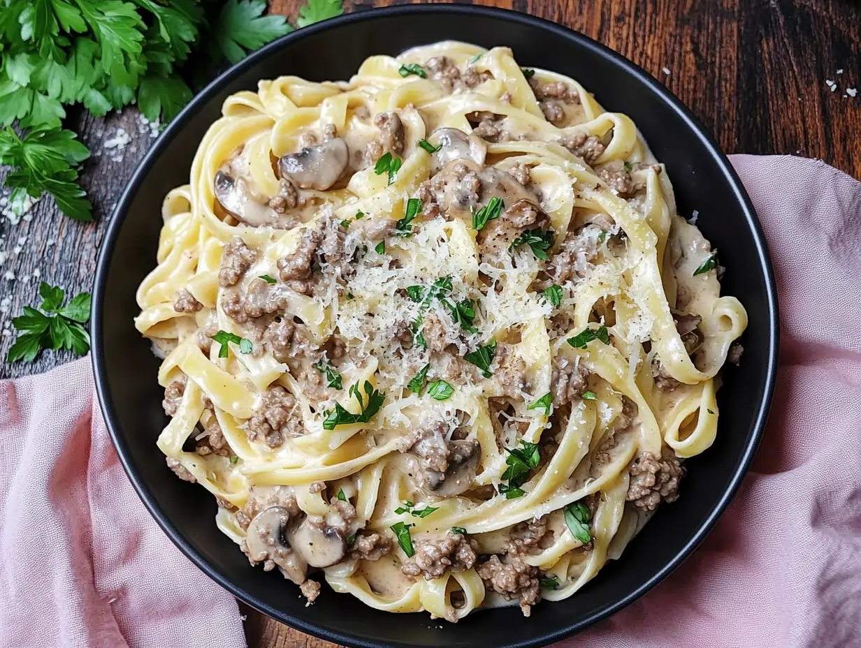 Creamy ground beef pasta Alfredo in a black bowl, topped with fresh parsley and grated Parmesan