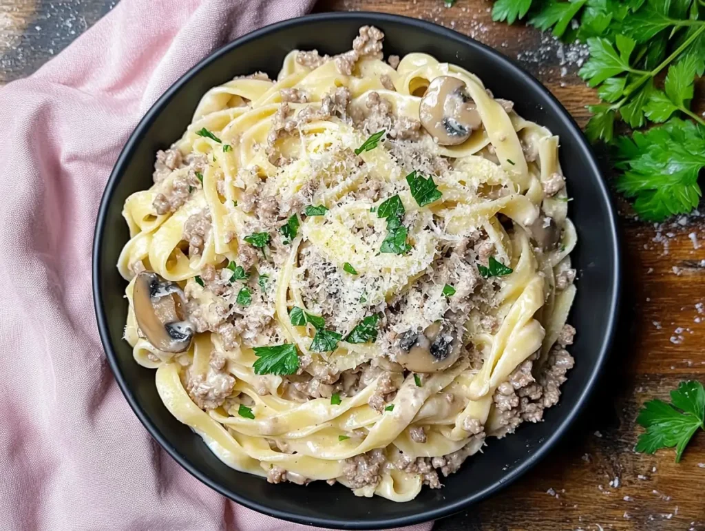 Rich ground beef pasta Alfredo with mushrooms and parsley, served on a rustic wooden table.