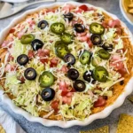 Homemade taco dip garnished with fresh toppings and paired with tortilla chips for dipping.