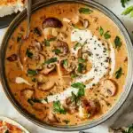 Creamy Hungarian mushroom soup garnished with fresh parsley and a drizzle of cream, served with crusty bread.