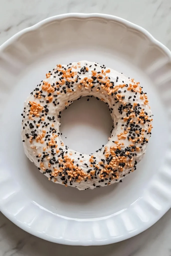 Unbaked high-protein bagel dough topped with everything bagel seasoning on a white plate.