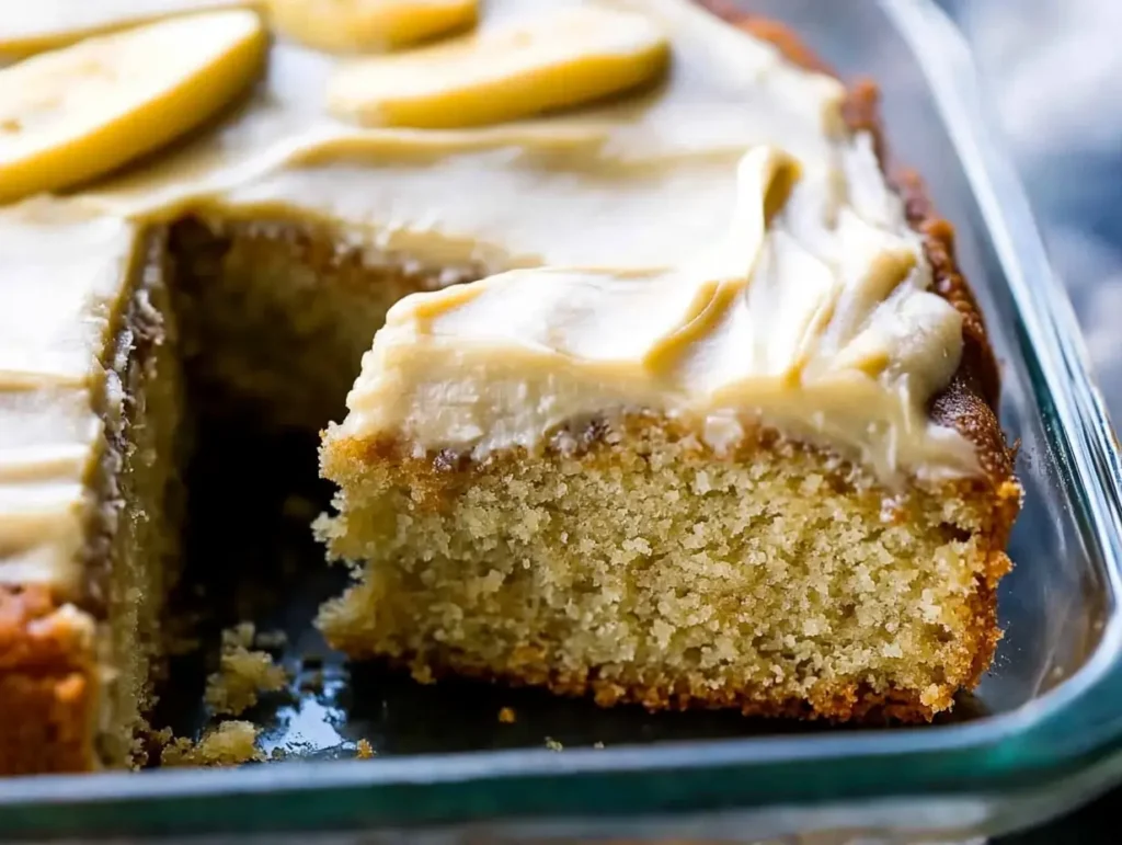 A moist slice of banana cake topped with creamy frosting, served in a glass baking dish.