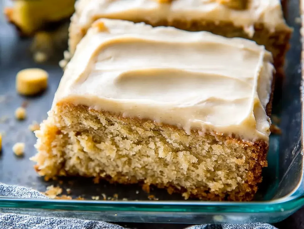 Homemade banana cake with rich cream cheese frosting, highlighting its moist texture and golden edges.
