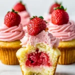 Strawberry cheesecake cupcakes with creamy pink frosting, fresh strawberries on top, and a delicious strawberry-filled center.