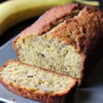 Freshly sliced banana bread on a metal tray with a ripe banana in the background.