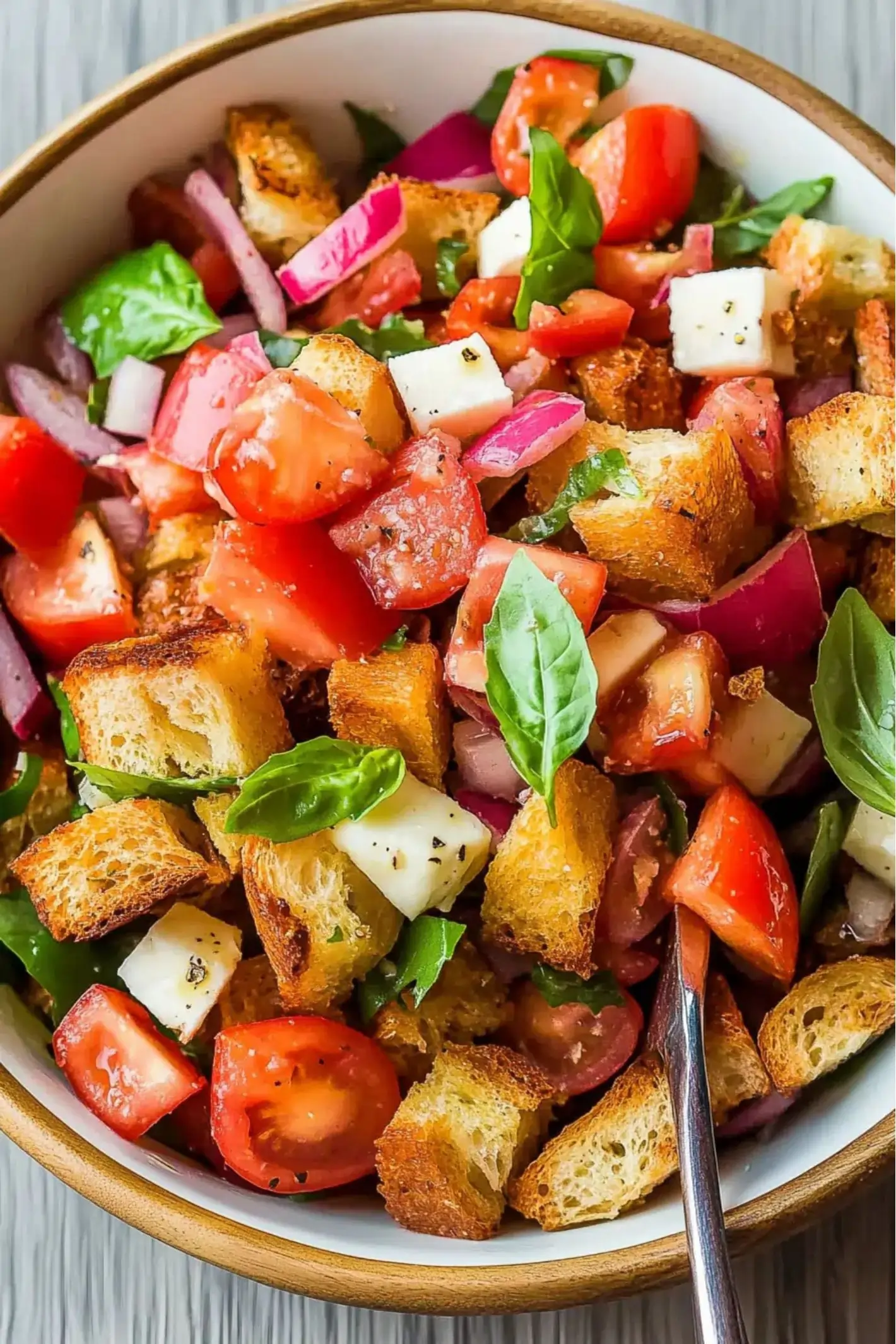 Close-up of a fresh Panzanella salad with crispy toasted bread cubes, juicy cherry tomatoes, red onion, mozzarella, and basil, tossed in a light dressing in a white bowl.